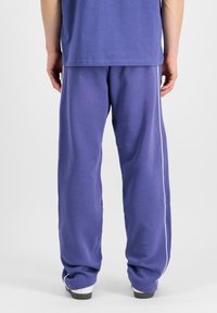 Lila udobna trenirka s stranskimi belimi črtami. Narejena iz mehkega materiala, z elastičnim pasom in ohlapnim krojem.