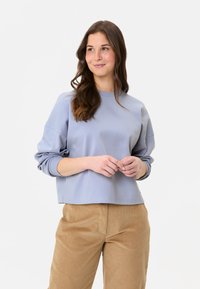 Helles blaues, kurzes Sweatshirt mit rundem Halsausschnitt und gerafften, weichen Ärmeln, kombiniert mit beige Cordhosen. Glatte Textur, lässiges Design.