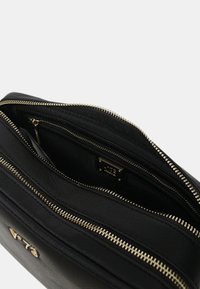 Borsa in pelle nera con superficie texture, presenta due scomparti, cerniere dorate e un accento logo discreto.