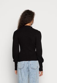 Czarny prążkowany sweter z dopasowanym korpusem i bufiastymi rękawami, zestawiony z jasnoniebieskimi, wysokim stanem jeansami. Minimalistyczny design i fakturowana tkanina.