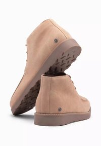 Botines de ante beige hasta el tobillo con punta redondeada, diseño con cordones y suela de goma texturizada que presenta un patrón de relieve; acento con logo en el lateral.