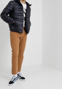 Marinblå puffjacka med horisontell quiltning, dragkedjestängning och huva; matchad med beige chinos och svart-vita sneakers.