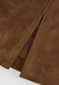 Tessuto in camoscio marrone che mostra da vicino una fessura con dettaglio delle cuciture, rivelando una fodera interna contrastante. Texture morbida e finitura opaca.