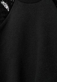 Svart pullover med en slät textur; har en paljetterad svart detalj på ena axeln och en ribbad halslinning.