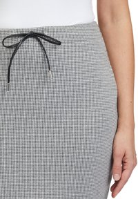 Spódnica w szaro-białą kratę houndstooth z czarnym sznurkiem do ściągania. Tkanina jest teksturowana, a sznurek ma srebrne akcenty na końcach.