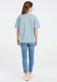 Lichtblauw oversized katoen t-shirt met korte mouwen, rechte zoom en minimale branding op de achterkant, gecombineerd met aansluitende lichtblauwe jeans.
