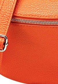 Oranje gestructureerde leren tas met een metalen rits. Het oppervlak is lichtjes gepolijst en toont een stevige, ronde vorm met zilverkleurige accenten.