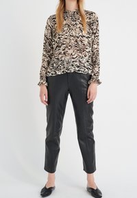 Blusa a maniche lunghe in un motivo astratto beige e marrone con colletto arricciato, abbinata a pantaloni tapered in pelle nera e scarpe slip-on nere.