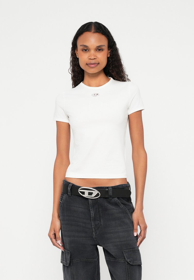 Balta pieguloša T-krekls ar apaļu kakla izgriezumu un īsām piedurknēm, ar nelielu sudraba logotipa akcentu. Kombinēts ar melnām, augsta vidukļa kravas biksēm.