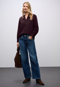 Bordowa bluzka z długim rękawem i wyciętym kołnierzykiem, zestawiona z jasnoniebieskimi spodniami z szerokimi nogawkami. Brązowe zamszowe botki za kostkę i brązowa torba na ramię.