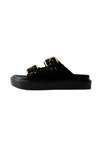 Sandale à glissière en suede noir avec deux accents de boucles dorées, de larges sangles et une semelle épaisse en noir. Texture lisse dans l'ensemble.