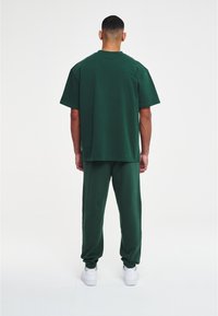 Groene katoenen T-shirt en bijpassende broek, ontspannen pasvorm, eenvoudig ontwerp. T-shirt heeft een ronde hals; broek heeft elastische boorden. Witte sneakers.
