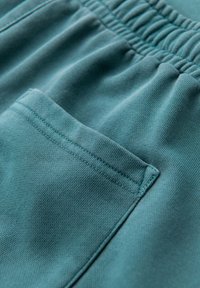 Nahaufnahme von mintgrünem Stoff mit einem elastischen Bund und einer quadratischen Tasche mit sichtbaren Nähten auf weichem, strukturiertem Material.