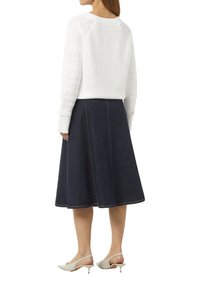 Witte gebreide trui met textuurontwerp en lange mouwen, gecombineerd met een donkerdenim A-lijnrok met contrasterende stiksels en een uitlopende vorm.