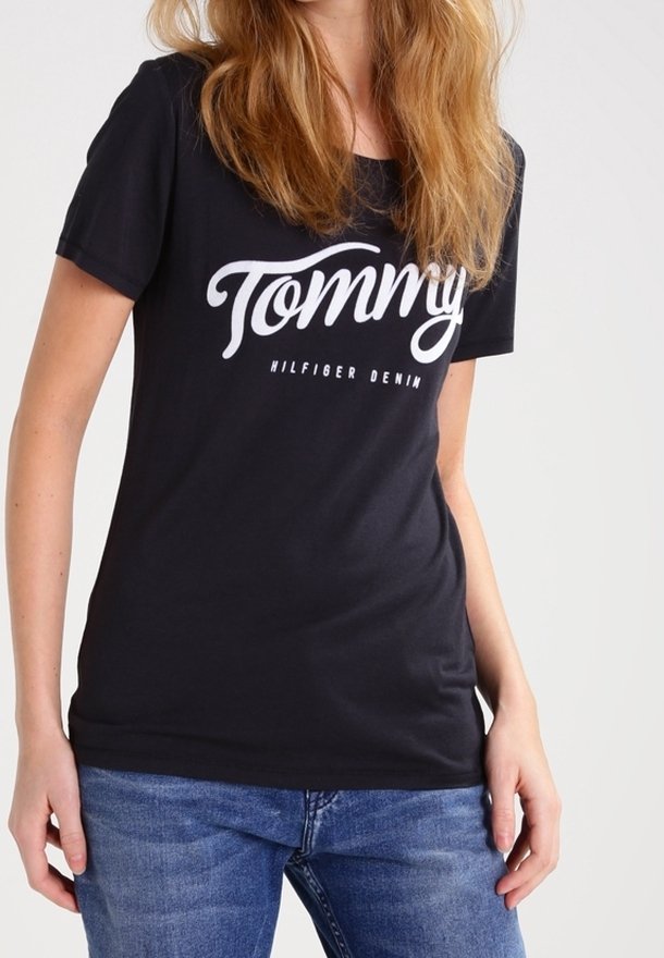 Camiseta de algodón negra con mangas cortas, que presenta un gran texto en blanco en forma de script "Tommy" y "Hilfiger Denim" debajo. Corte clásico, textura suave.