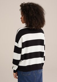Maglione con bold righe bianche e nere, in materiale lavorato, vestibilità rilassata, scollatura a girocollo e maniche lunghe, abbinato a jeans blu.