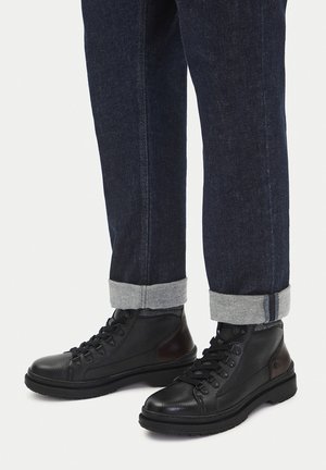 Czarne skórzane botki za kostkę z teksturowanym wykończeniem, okrągłym noskiem, wiązaniem na sznurowadła i gumową podeszwą. Połączone z podwiniętymi ciemnymi jeansami.