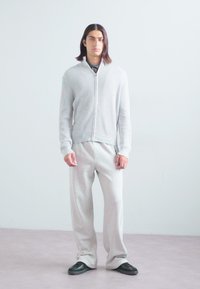 Ljusgrå ribbad zip-up tröja med långa ärmar, parat med matchande löst sittande sweatpants och mörka avslappnade skor.