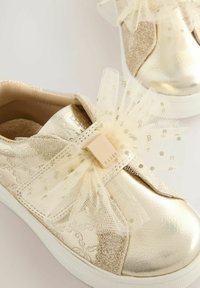 Goldene metallische Turnschuhe mit strukturierter Oberfläche, ausgestattet mit einer großen Tüll-Schleife und einem Verschluss-Akzent in der Mitte. Glatte Gummisohle.