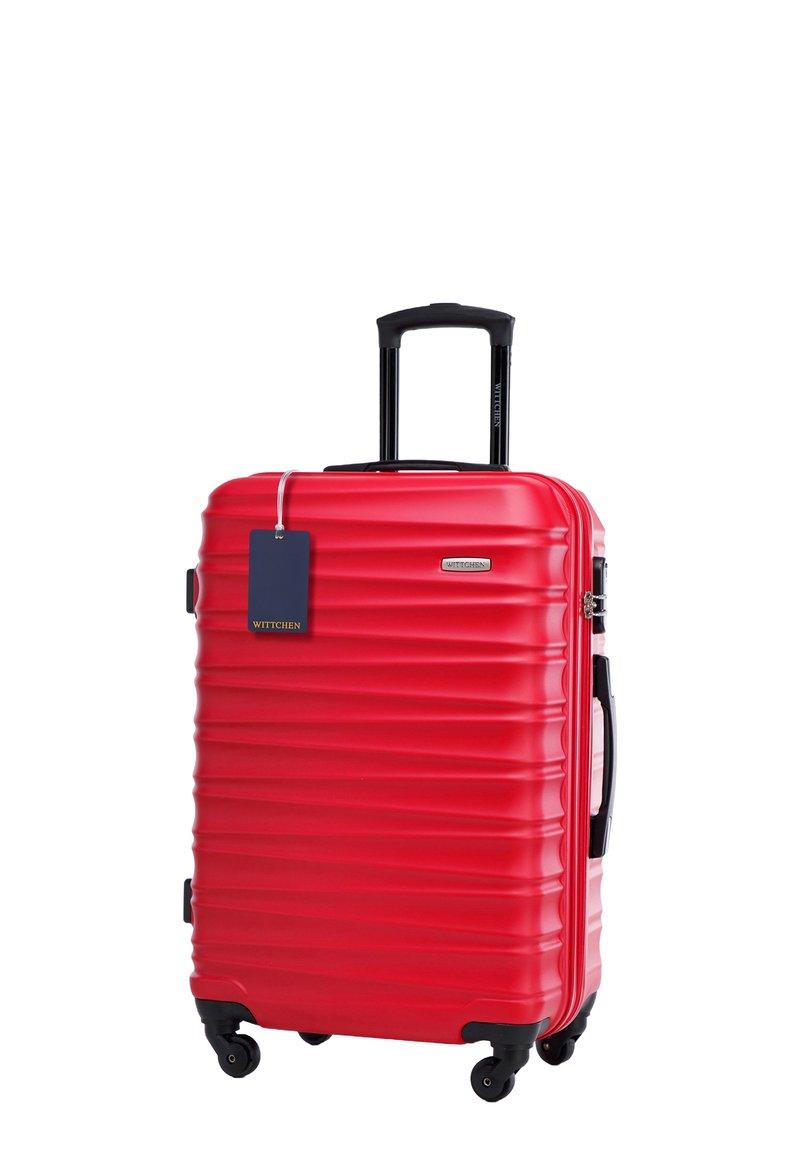 Valigia rigida rossa con texture rigata, manico nero retrattile, quattro ruote e un'etichetta blu. Il materiale è resistente e leggero.