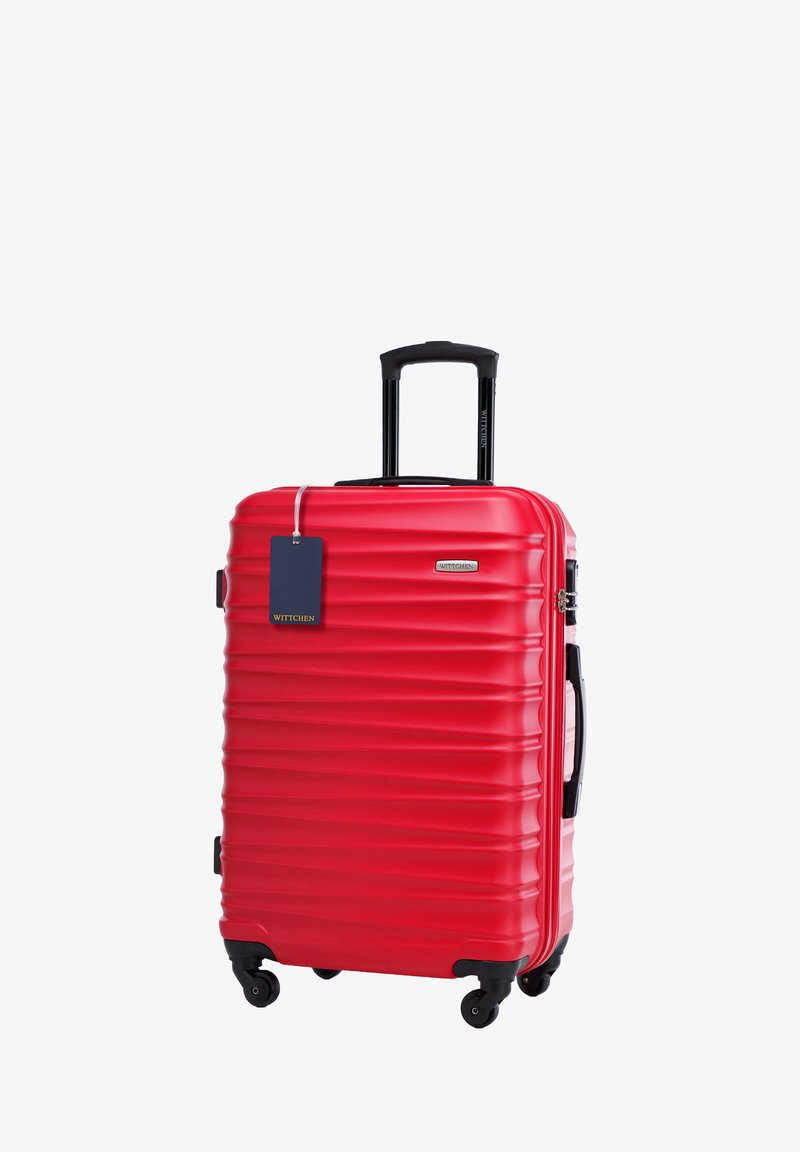 Valigia rigida rossa con texture rigata, manico nero retrattile, quattro ruote e un'etichetta blu. Il materiale è resistente e leggero.