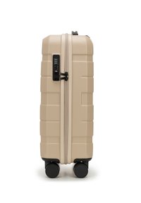 Valigia rigida beige con superficie testurizzata, dotata di combinazione di chiusura, zip resistente e quattro ruote nere per la mobilità.