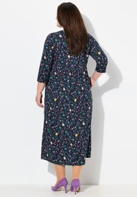 Kleid mit floralem Muster in Dunkelblau, drei Viertelärmeln, gerafftem Bund und mittellangem Saum; kombiniert mit lila High Heels.