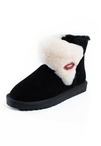 Botas de tobillo de ante negro con un puño de piel sintética blanca, que presentan un acento en forma de labio rojo. Suela de goma plana, punta redonda y textura acogedora.