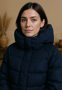 Marineblauwe pufferjack met een hoge kraag, voorzien van een doorgestikt ontwerp en een gladde textuur. De jas is geïsoleerd en heeft een ritssluiting aan de voorkant.