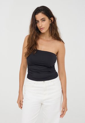 Top nero senza spalline con un design arricciato, indossato con jeans bianchi a vita alta. La texture liscia e la forma aderente esaltano la silhouette.