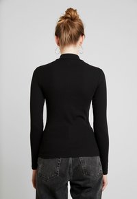 Svart långärmad topp med ribbat mönster och hög krage, tillsammans med högmidjade mörkgrå denimjeans.