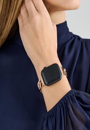 Smartwatch z kwadratowym czarnym ekranem, metalowymi ogniwami w różowym złocie, noszony na nadgarstku. Materiał w głębokim granacie z subtelną teksturą.