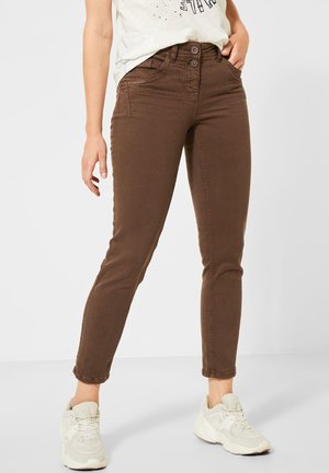 Braune Slim-Fit-Hose mit Doppelknopfverschluss, getragen mit cremeweißen Sneakern und einem in die Hose gesteckten weißen T-Shirt mit Aufdruck.