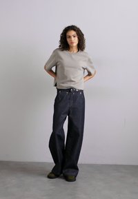 Un haut gris à manches courtes avec une coupe décontractée, associé à un jean en denim à jambes larges bleu foncé et des chaussures à semelle verte. Design simple, détails minimalistes.