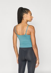 Een aansluitend teal tanktop met dunne bandjes, gecombineerd met zwarte leggings met hoge taille. De stof oogt glad met een lichte glans.