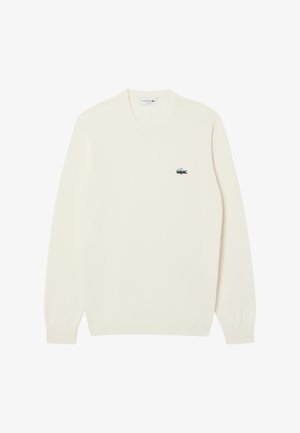 Suéter de color crema con un escote redondo y puños acanalados. Presenta un pequeño logo de Lacoste en azul y verde en el lado izquierdo del pecho.