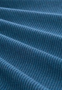 Primo piano di un tessuto in maglia a coste blu che mostra una texture piegata e linee verticali in un materiale morbido.