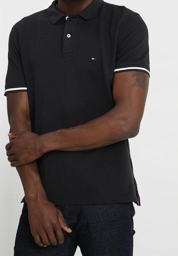 Polo noir avec bordure blanche sur le col et les manches. Petit logo sur la poitrine. Manches courtes, tissu en coton, coupe droite.