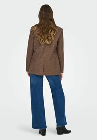 Bruine blazer met textuur en een aansluitend ontwerp, met een enkele rugventilatie, gecombineerd met blauwe wijde jeans en zwarte enkellaarsjes met hak.