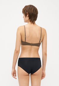 Bra in brown with adjustable straps and hook closure; paired with black high-waisted briefs. Sleek, smooth fabric with minimal details.