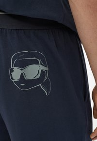 Mornarsko plavi šorts imaju elastičnu gumicu u struku i svijetlosivu grafiku osobe sa sunčanim naočalama otisnutu na lijevoj nozi.