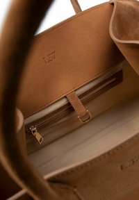 Tan suède handtas interieur met een ritsvak, gouden hardware en een platte insteekzak. Voorzien van een minimalistisch ontwerp met een geperste logo.