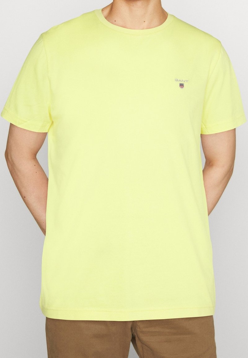 T-shirt à manches courtes et col rond en coton jaune vif, présentant un petit logo de marque sur la poitrine gauche et une texture lisse.