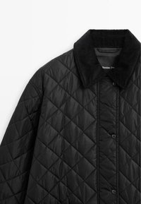 Schwarze gesteppte Jacke mit einem Cordkragen, Druckknopfverschluss und einem Rautenmuster über den Stoff.