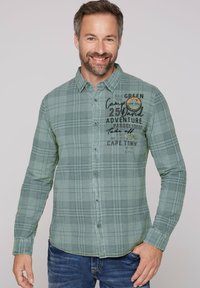 Camisa de mangas largas a cuadros verdes con botones en el frente, con gráficos de texto en el pecho. Tejido suave con dobladillo curvado y puños abotonados.