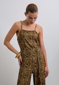 Mono floral con tirantes finos, presenta un patrón en tonos marrón y amarillo, tejido ligero y una cintura atada para un ajuste entallado.