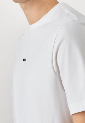 Mand iført en simpel hvid kortærmet t-shirt med lille sort "BOSS" logo på venstre bryst, vist fra skulder til nakke.