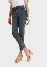 Jeans de mezclilla oscuros de cintura alta con un corte tapered, combinados con tacones de plataforma en color beige, tejidos, que cuentan con correas cruzadas y tacones gruesos.