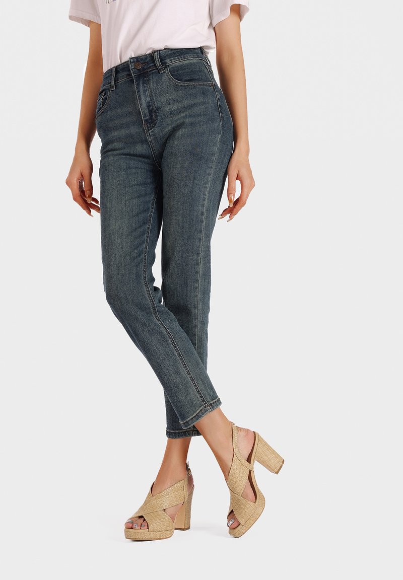 Jeans de mezclilla oscuros de cintura alta con un corte tapered, combinados con tacones de plataforma en color beige, tejidos, que cuentan con correas cruzadas y tacones gruesos.