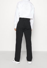 Vaqueros de mezclilla negra con un diseño de pierna recta, cintura alta y bolsillos traseros, combinados con una camisa blanca holgada y zapatillas blancas.